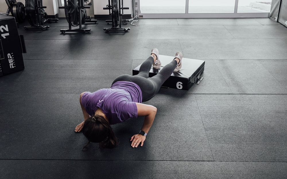 Female athlete performing deficit push-ups with her feet elevated on a 6" REP Stackable Soft Plyo Box.