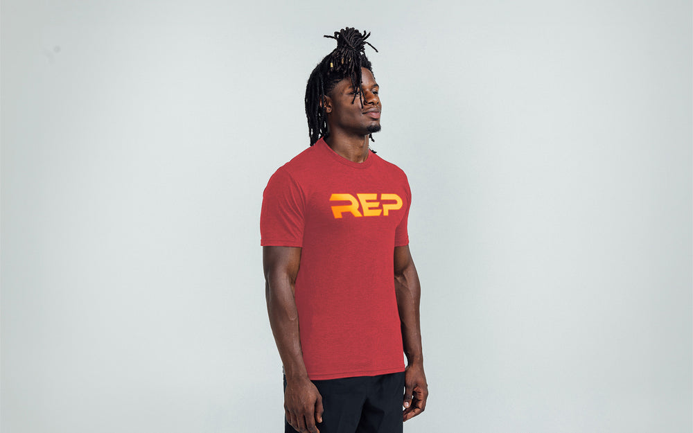 Model wearing the REP Fitness Men's Daily Driver 2.0 Tri-Blend Crew T-Shirt in Heather Red with a Gold graphic