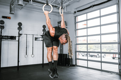 Athlete working out on REP Competition Gymnastic Straps and Wood Rings hanging from metal ceiling infrastructure
