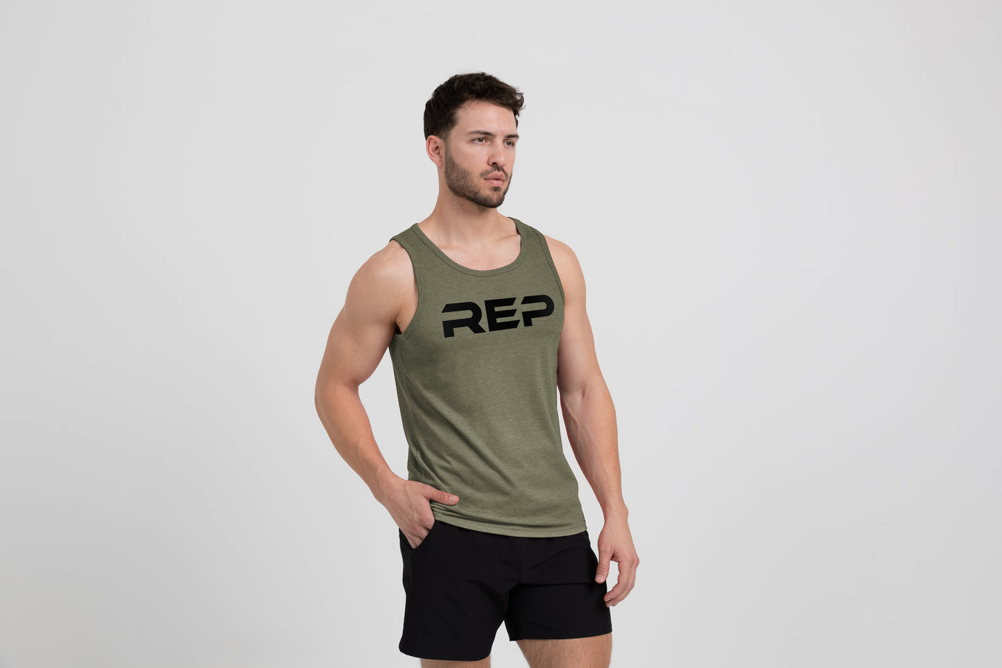 Man wearing the Men's Daily Driver Tri-Blend Tank in Heather Olive with shorts