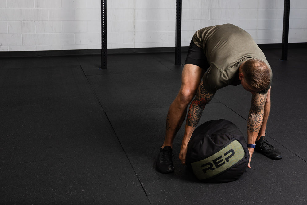 Person performing a workout with a Rep Fitness stone sandbag in a gym setting
