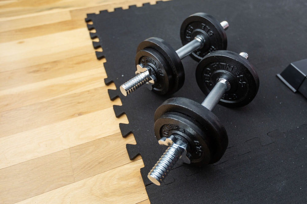 Adjustable dumbbells sitting on top of Rubber Floor Tiles on a wood floor