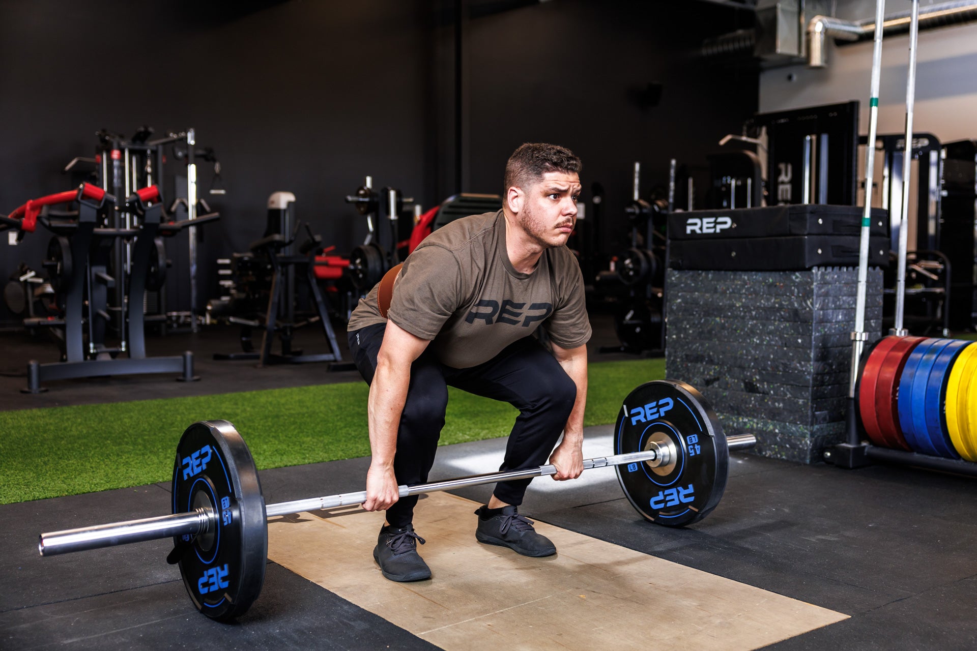 Action shot: Athlete in a ready position grips a barbell loaded with a pair of REP 45 lb Sport Bumper Plates 2.0