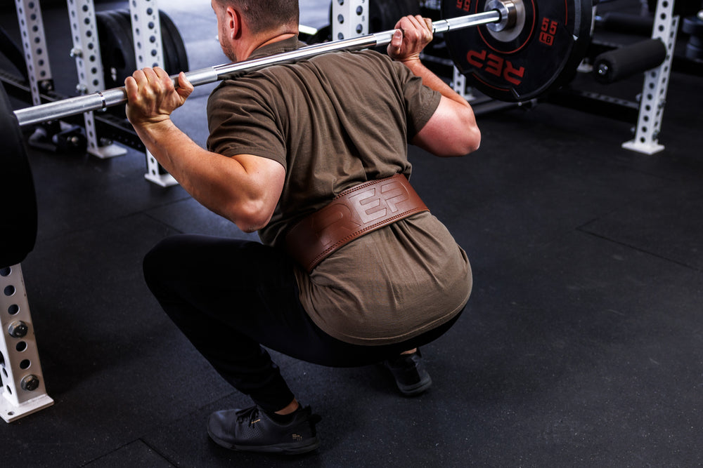 Action-shot: Athlete at the deepest point of a squat wearing a brown REP Leather Lifting Belt around their waist
