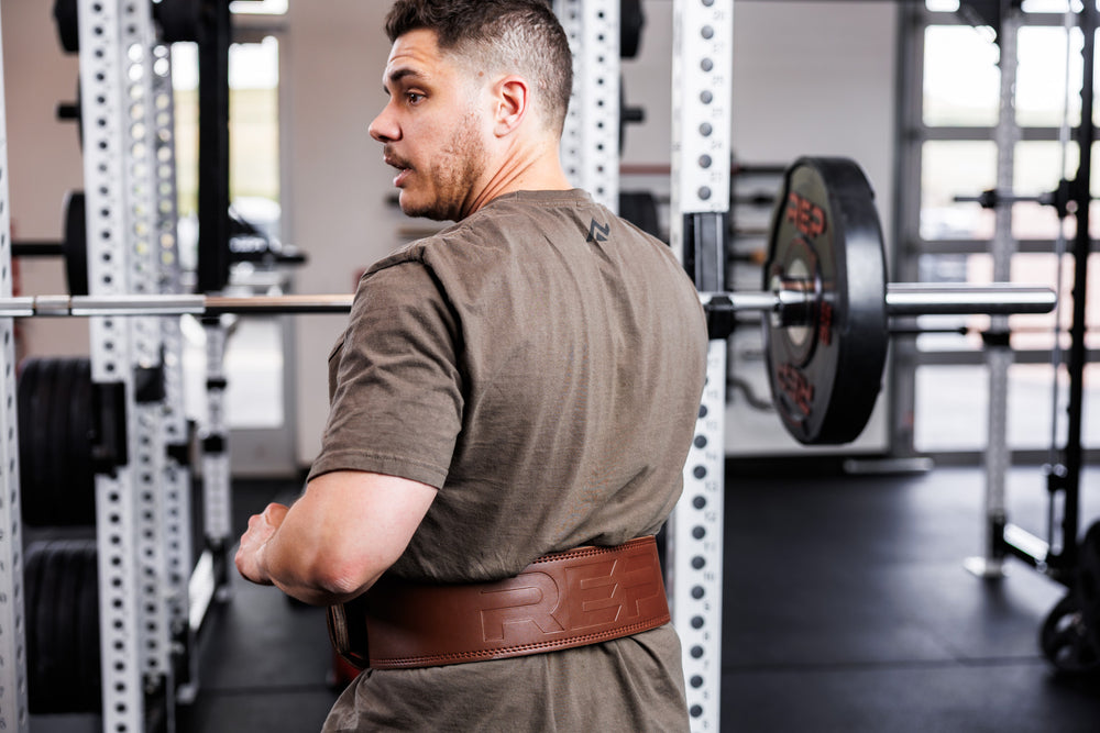 Back-shot: Athlete wearing a brown REP Leather Lifting Belt standing in front of a PR-5000 rack