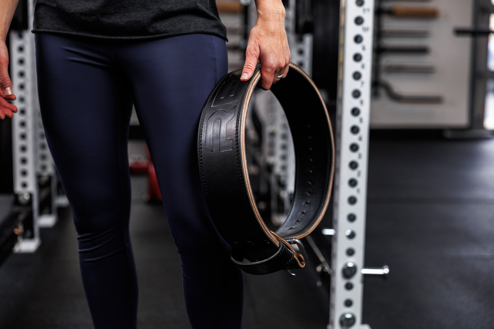 Close-Up: Athlete holding the REP Leather Lifting Belt in Black at hip level before putting it on