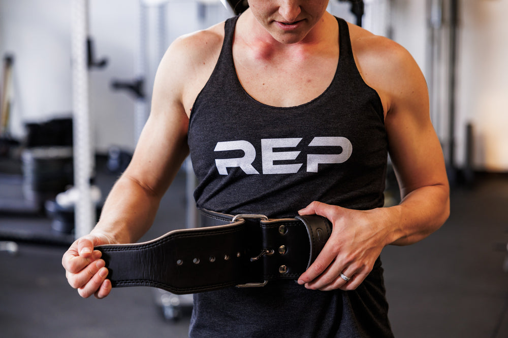 Front-shot: Athlete tightening the black REP Leather Lifting Belt around their waist in a home gym setting