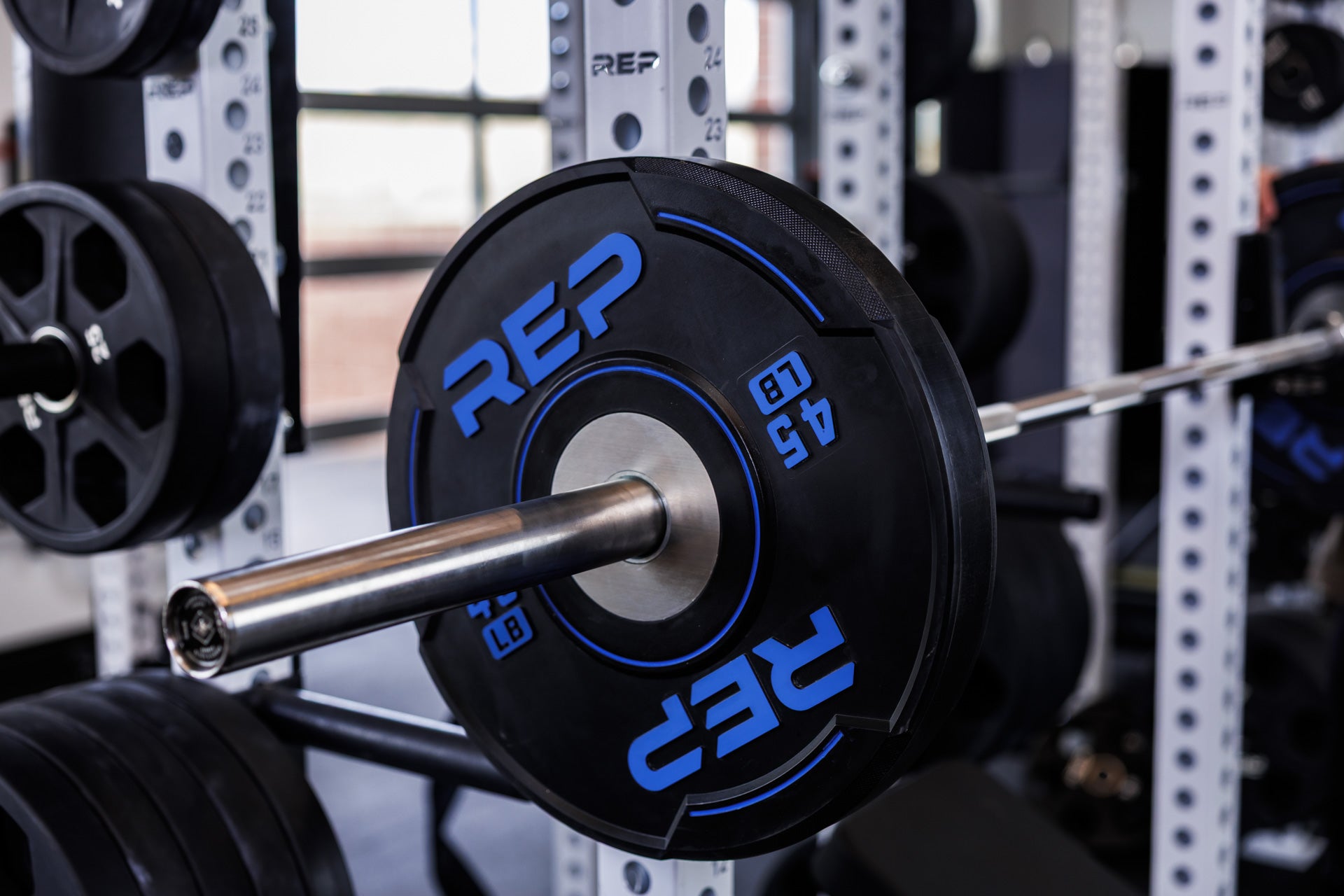 Close-up: Double Black Diamond Power Bar loaded with 45 lb REP Sport Plates 2.0 racked on the front of a PR-5000 Power Rack