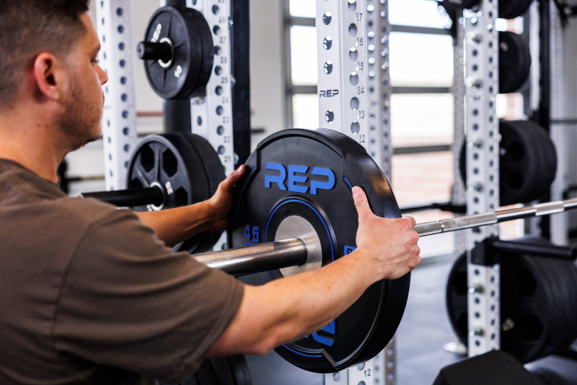 Action-shot: Athlete loading a barbell with a 45 lb REP Sport Plate 2.0 while racked on the front of a PR-5000 Power Rack
