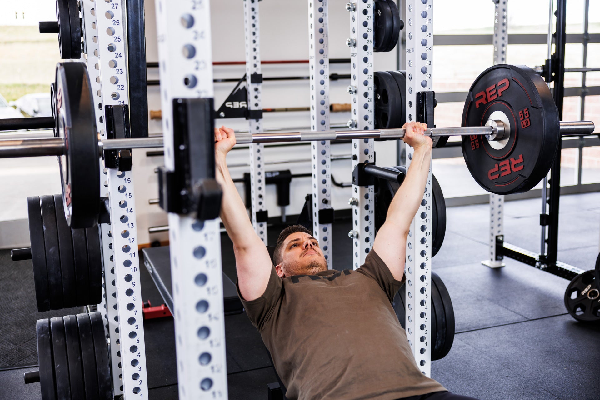Action-shot: Athlete holds barbell with 55 lb REP Sport Plates 2.0 in an incline bench position inside a PR-5000 Power Rack