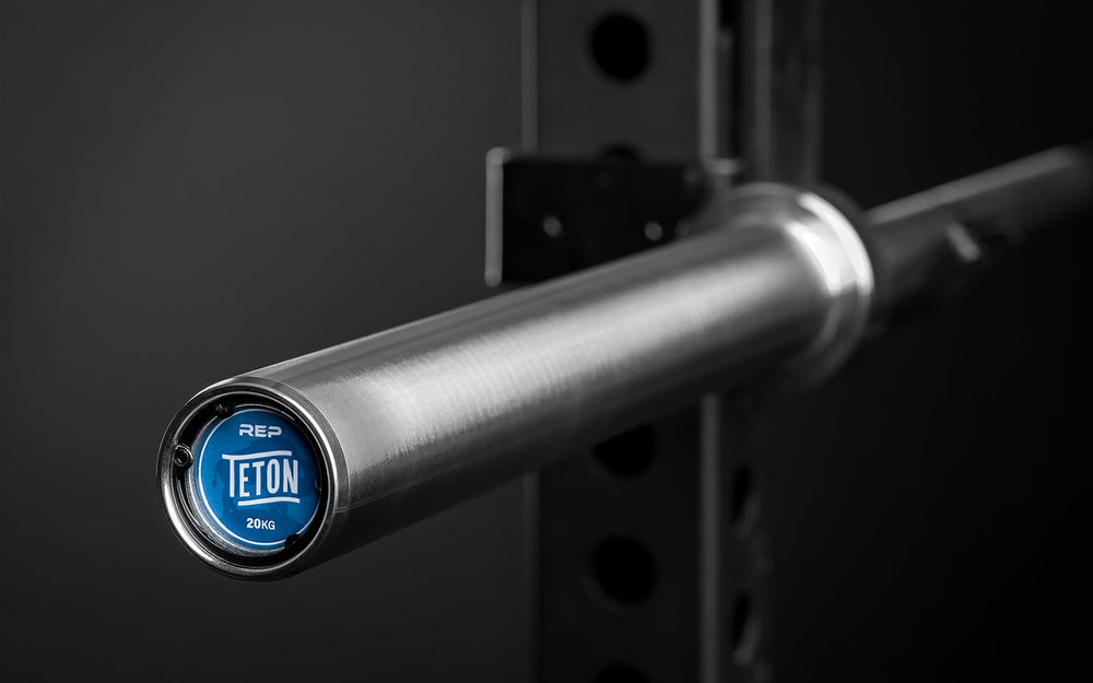 Close-up view of the sleeve and endcap sticker of a racked REP Teton Training Bar - 20kg.