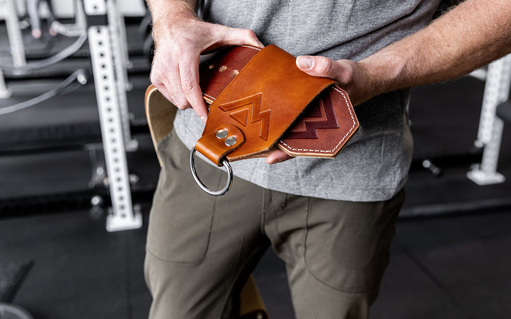 Athlete sliding a brown REP Leather Utility Loop onto a brown REP Premium Leather Lifting Belt.