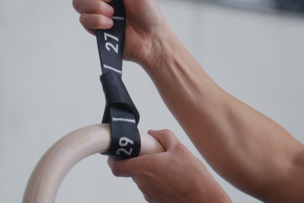 An athlete cinching the REP Competition Gymnastic Straps and Wood Rings before working out