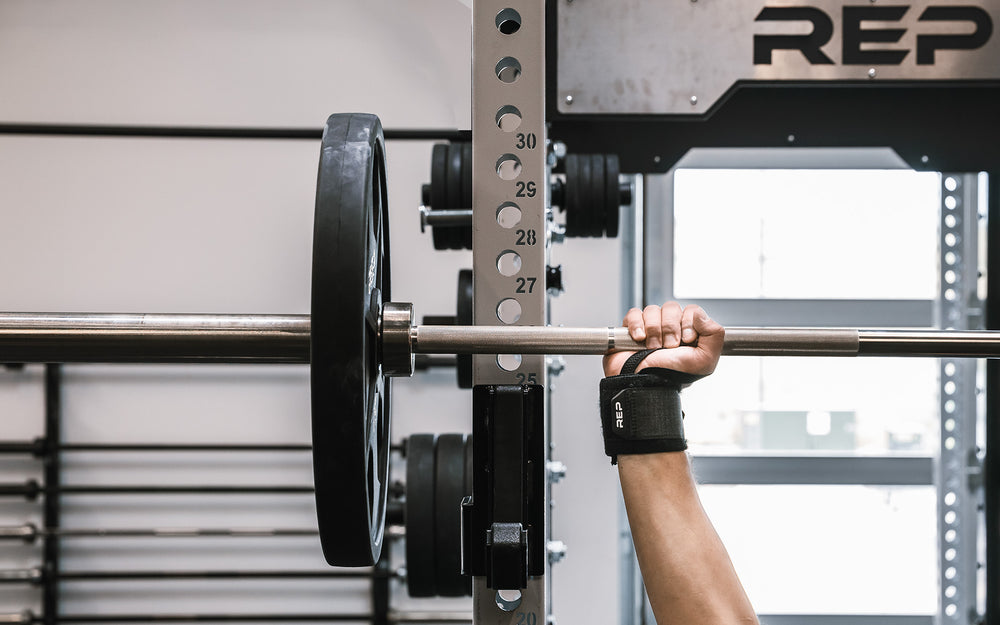 Close-up: Athlete's wrist being supported by the REP Wrist Wrap while pressing a loaded barbell