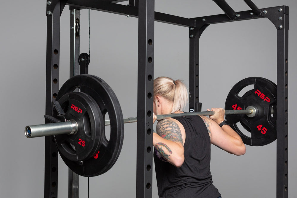 Lifter standing with a barbell loaded with a pair of 45lb and 25lb Rubber Coated Olympic Plates in the back rack position inside of a PR-1100 power rack.