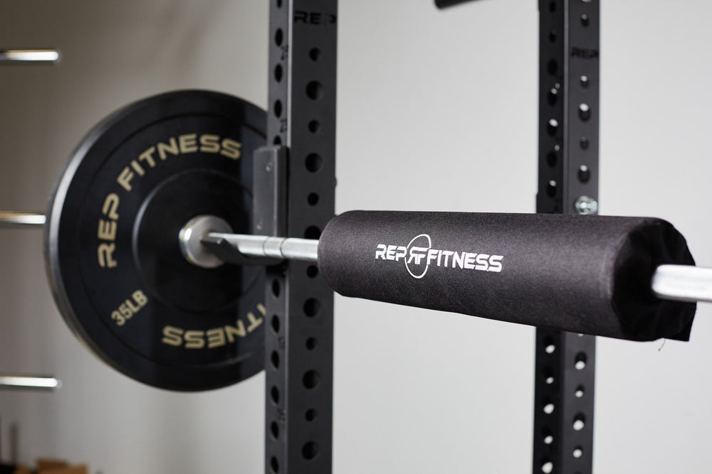 A REP barbell shoulder pad secured onto a racked barbell loaded with REP bumper plates.