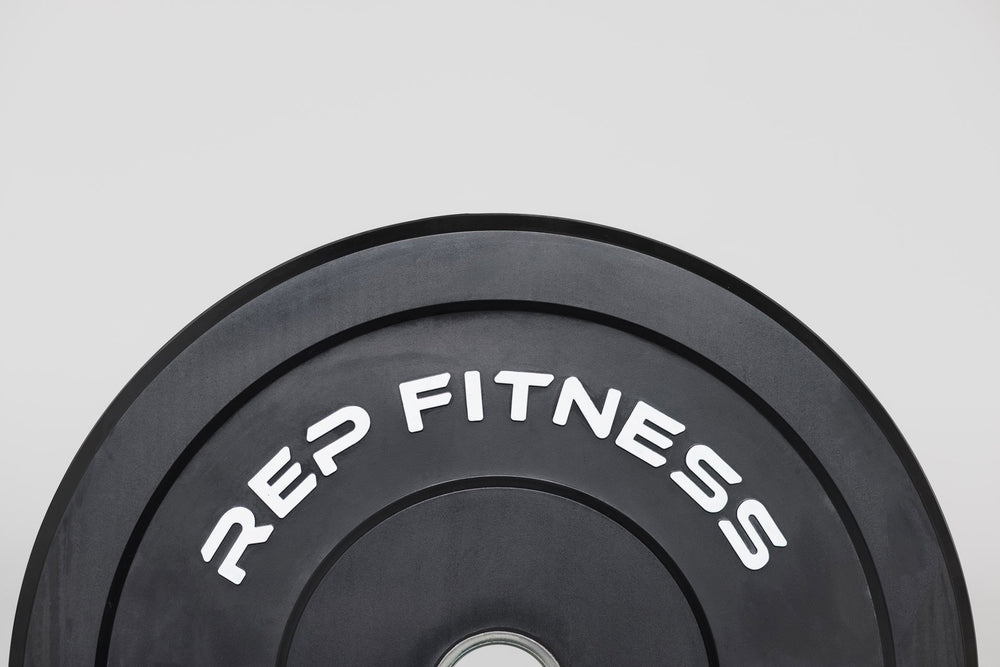 A top half view of a plate showing the white raised "REP FITNESS" lettering for a sharp contrast on the black bumper plate.