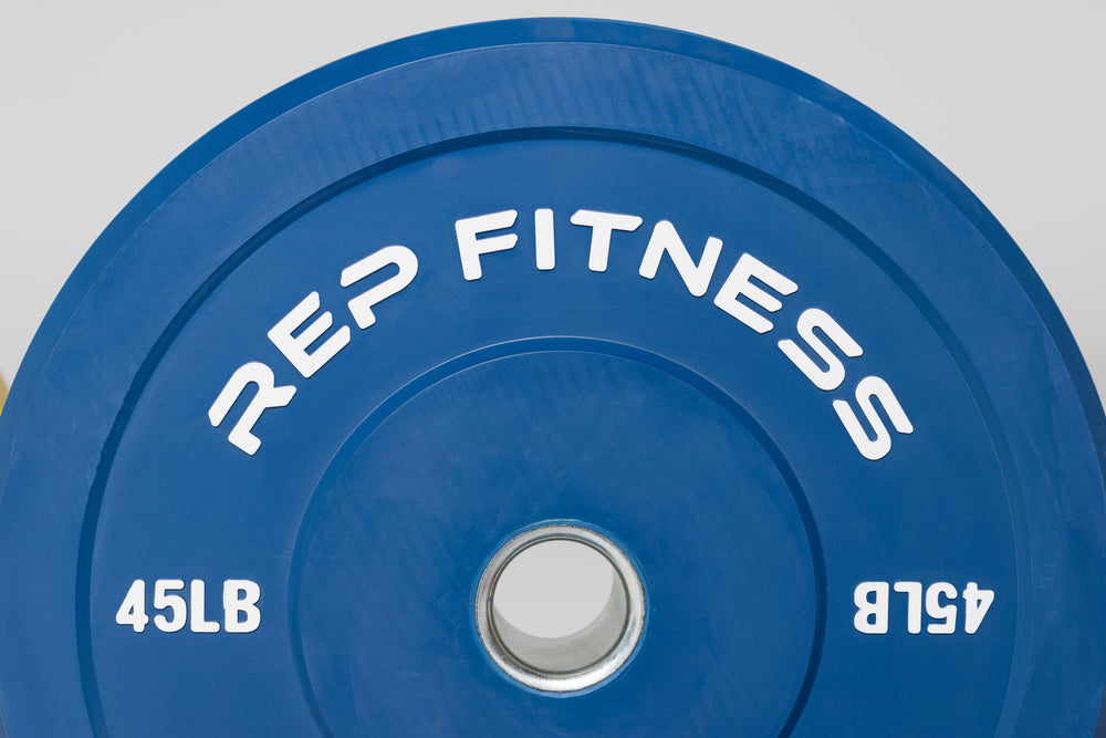 Close-up view of blue 45lb color bumper plate showing white raised "REP Fitness' and weight marking lettering.