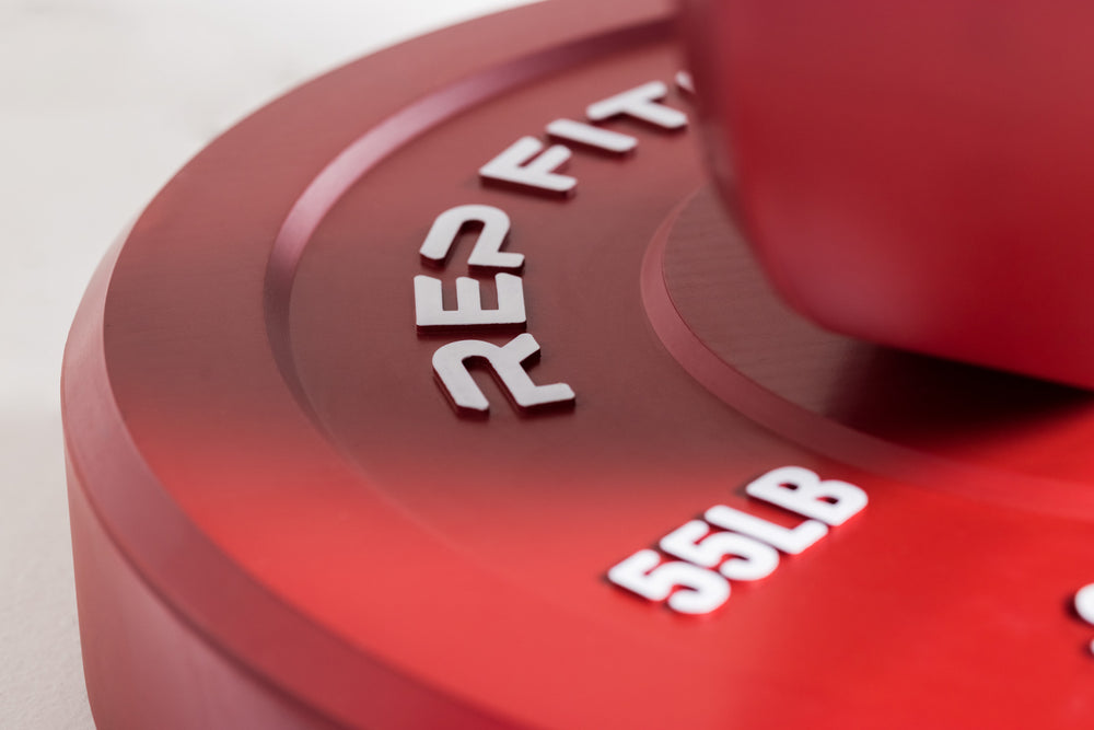 Close-up view of red 55lb color bumper plate showing white raised "REP" and weight marking lettering.