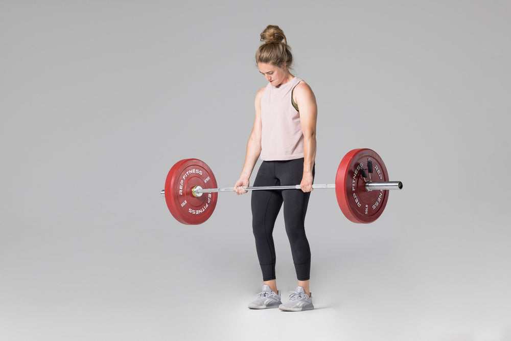 Lifter at the top position of a deadlift using a barbell loaded with a pair of red 55lb colored bumper plates.