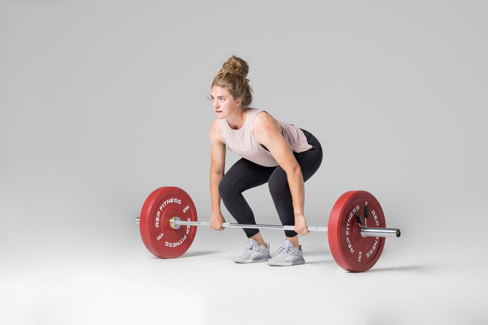 Lifter in set-up position to perform a clean with a barbell loaded with a pair of red 55lb colored bumper plates.