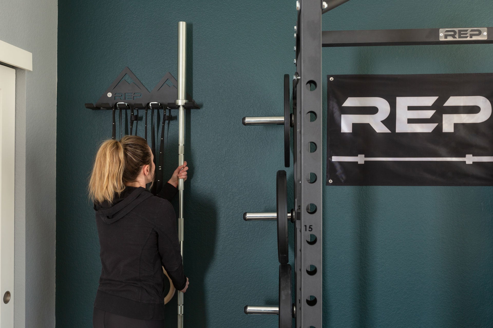Lifter in a home gym hanging up a barbell in the REP Multi-Use Wall Storage.