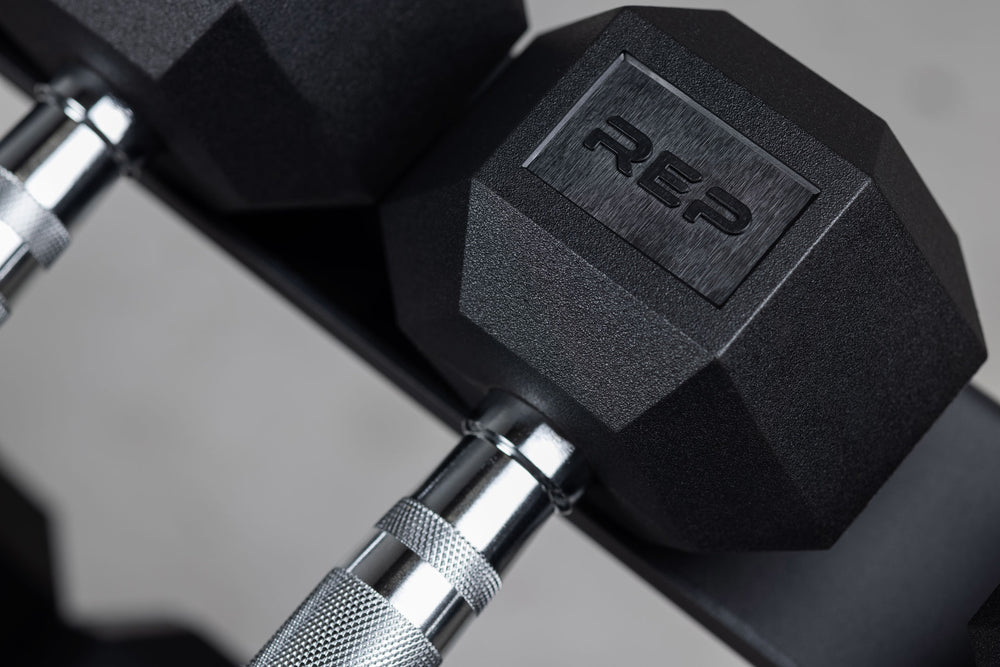 Close-up view of the "REP" logo on one side of the dumbbell head of an Ergo Hex Dumbbell stored on a REP Dumbbell Rack.