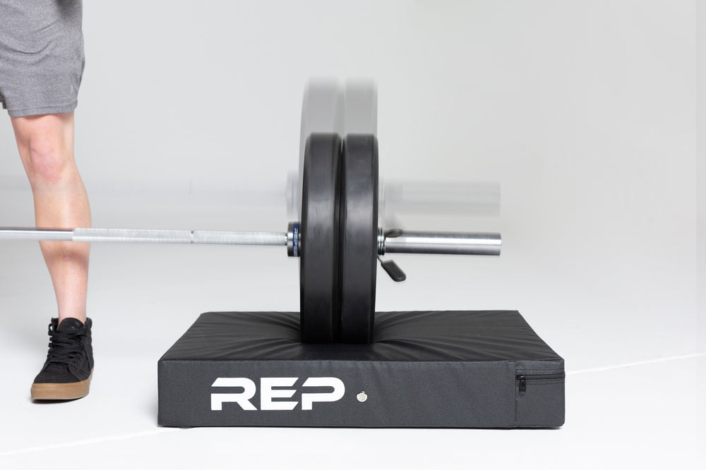 Close-up view of a loaded barbell making contact with a REP Crash Pad after having been dropped.