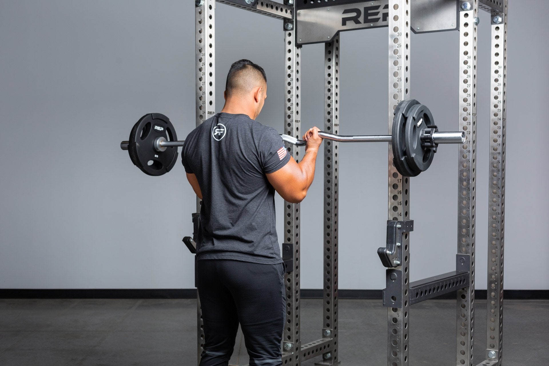 Lifter performing bicep curls with a loaded rackable curl bar from a PR-5000 rack.