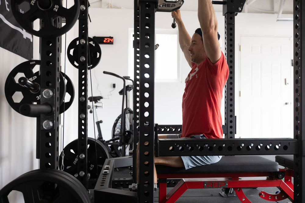 Lifter sitting on a bench inside of a PR-5000 rack performing lat pulldowns loaded with a pair of 35lb Urethane Coated Equalizer Plates.