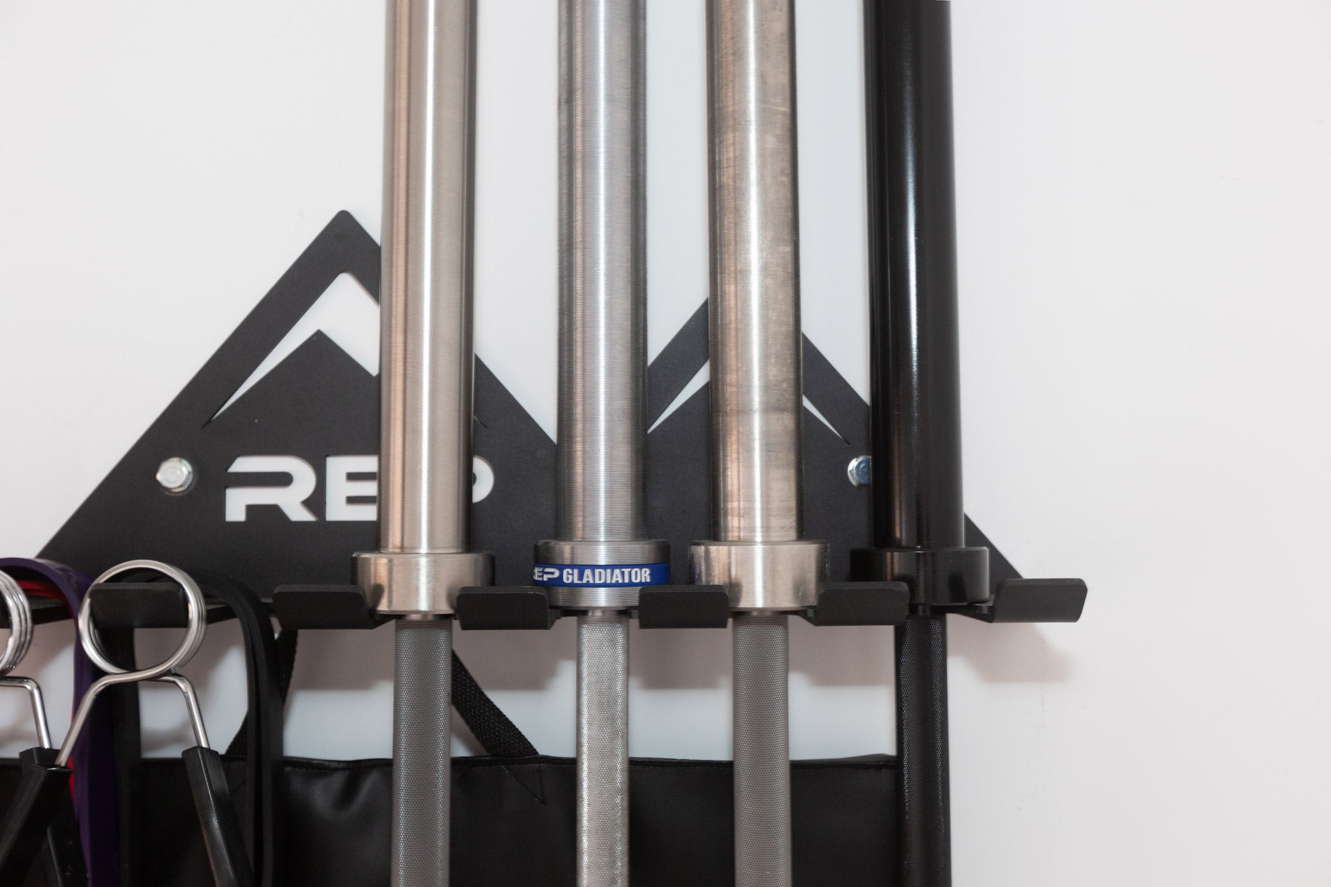Close-up view of exercise bands, spring clips, and barbells all being stored on the REP Multi-Use Wall Storage.