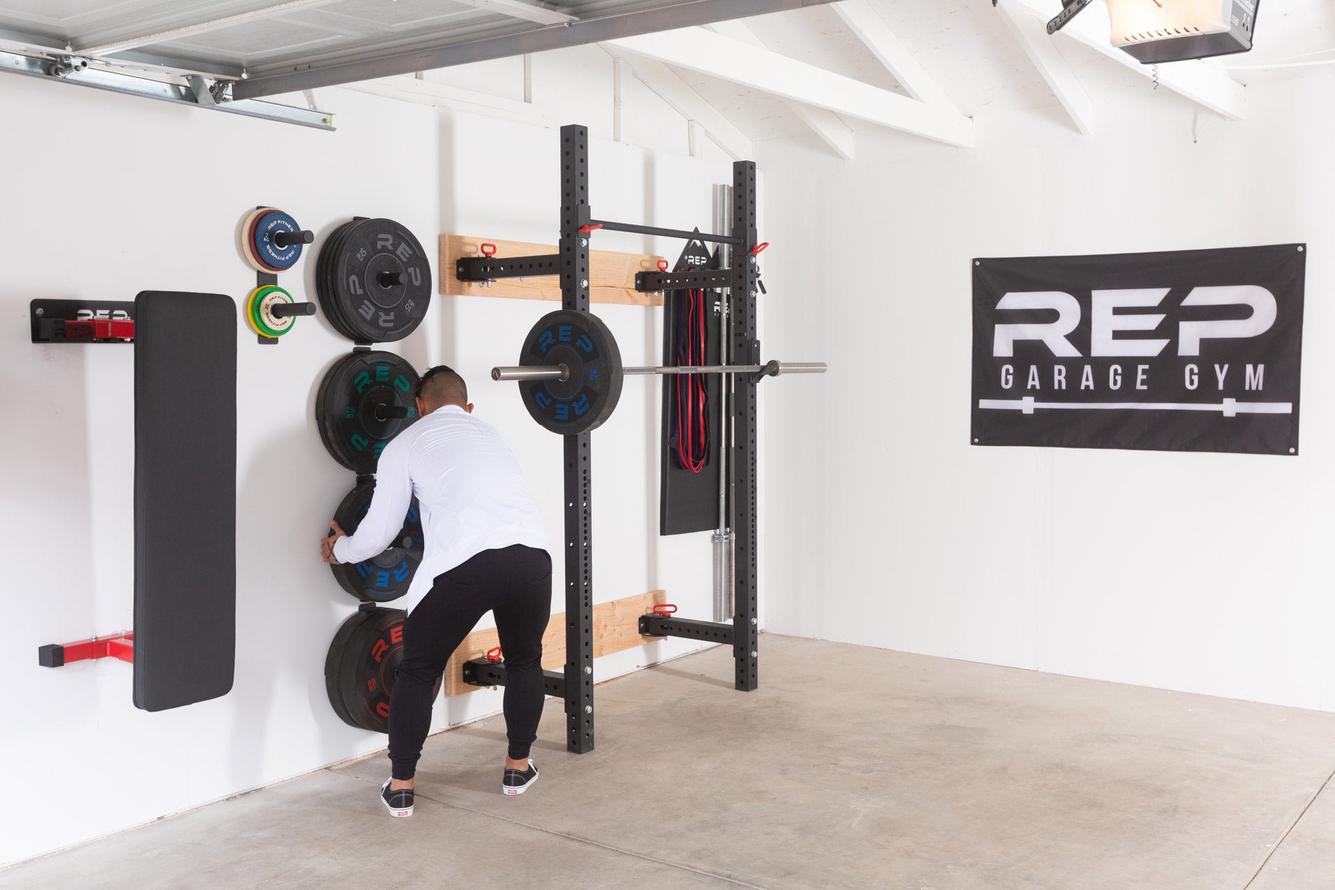 A lifter in a garage gym removing a 45lb bumper plate from a single Wall Mounted Plate Storage to put on a racked barbell.