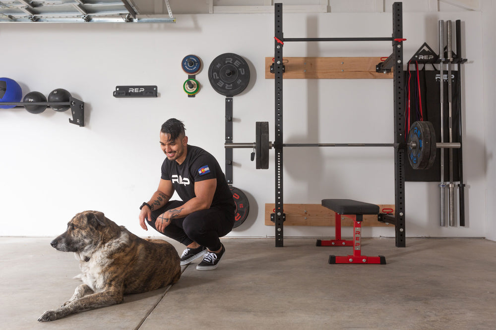 A lifter and his dog in a garage gym featuring a variety of REP space-saving equipment including single and double Wall Mounted Plate Storage.