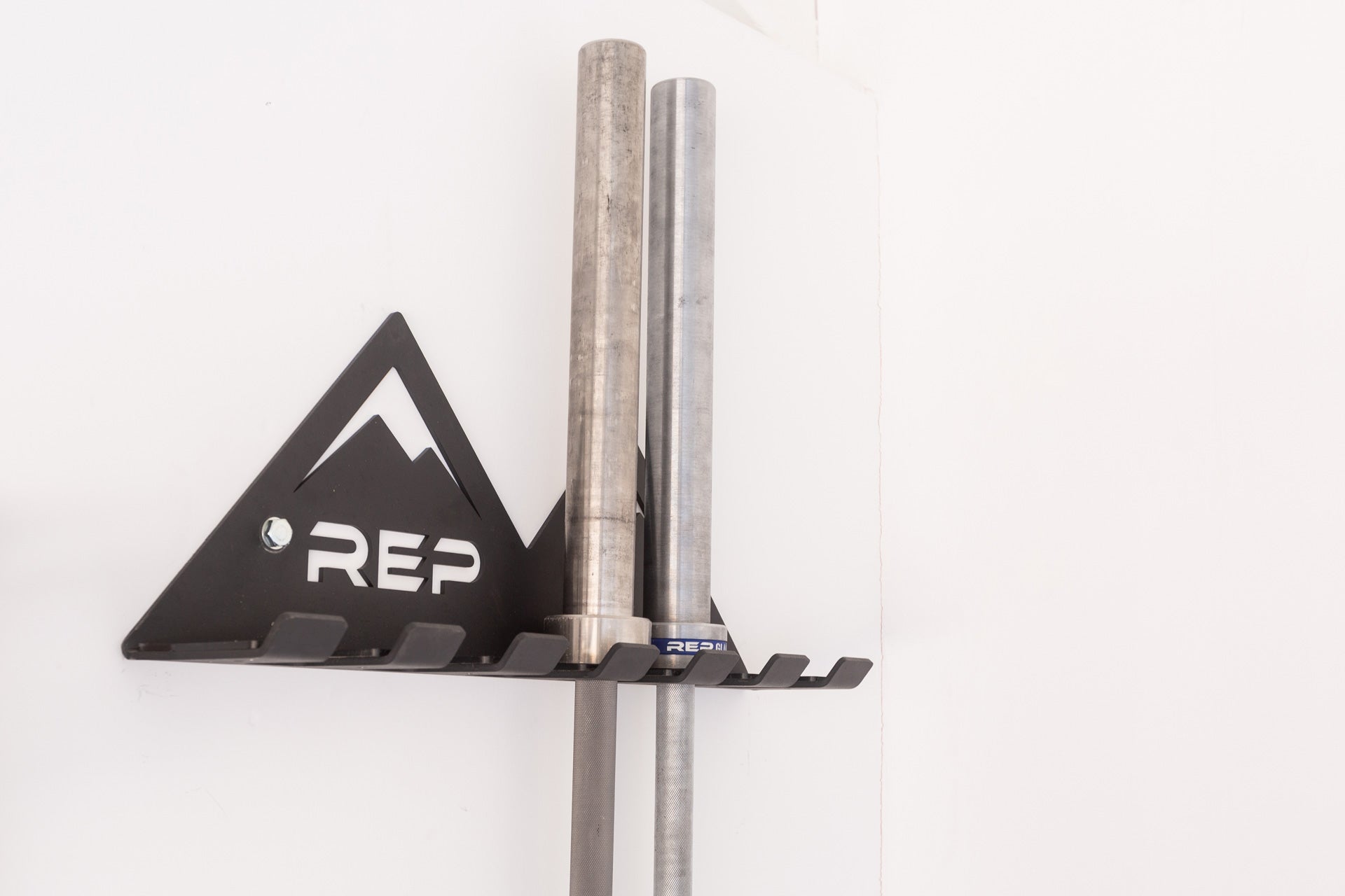 Close-up view of the REP Multi-Use Wall Storage storing two barbells.