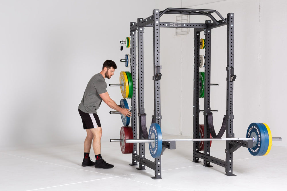 Lifter loading a barbell with Competition Bumper Plates (LB) onto a barbell resting on spotter arms attached to a PR-4000 rack.