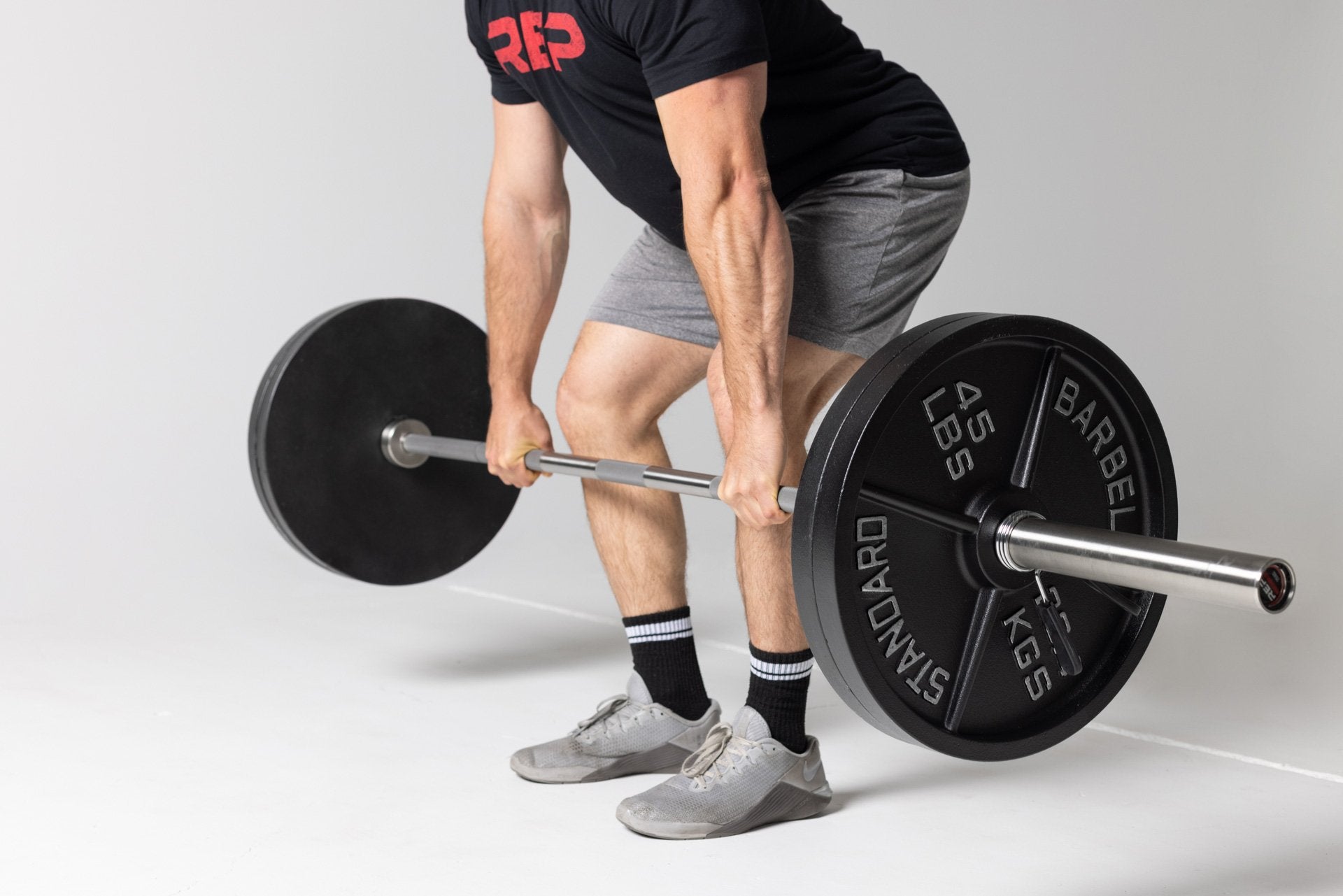Lifter performing a deadlift at just below knee level position using a barbell loaded with two pairs of 45lb Old School Iron Plates and spring clips.