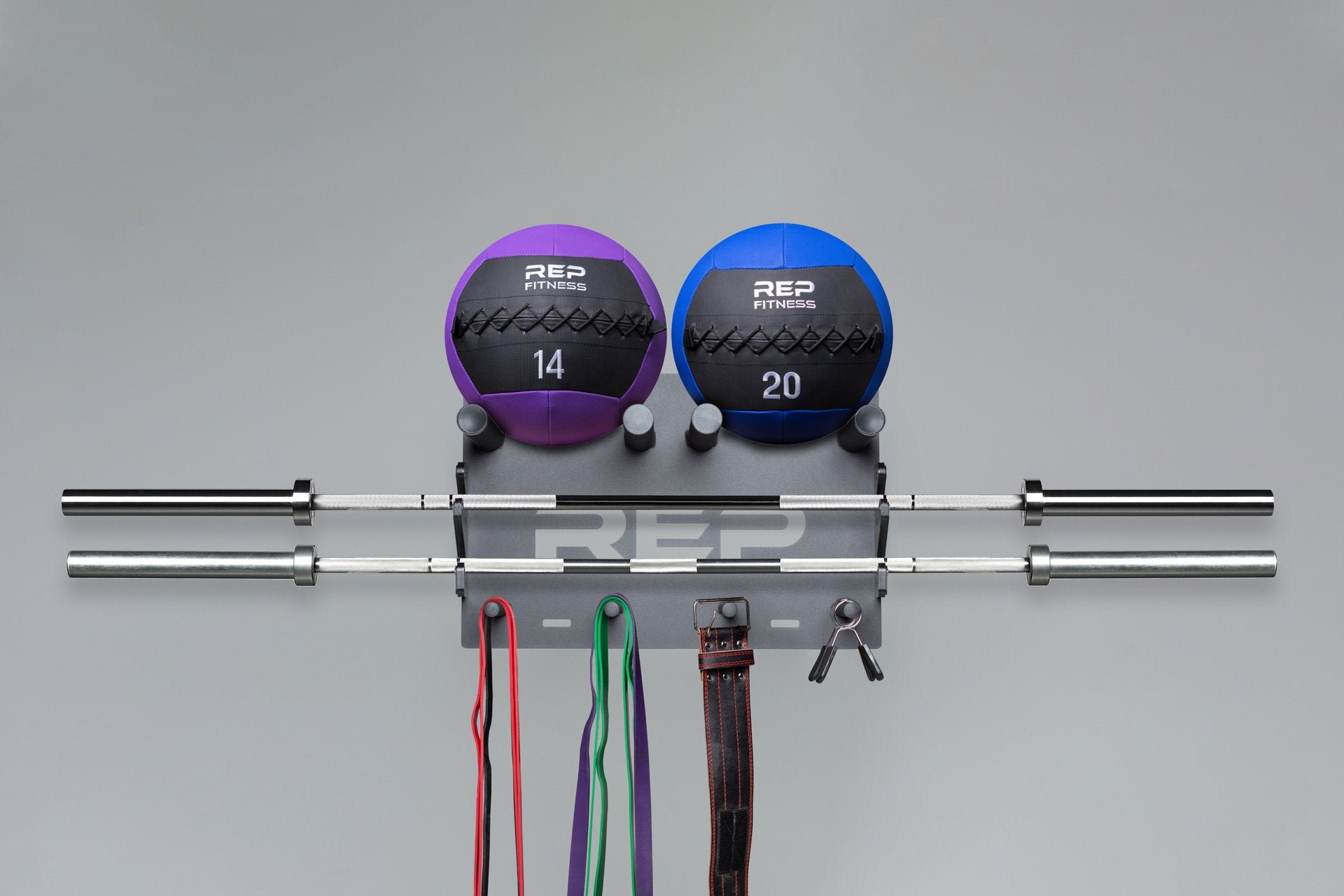 REP Wall Mounted Gym Storage Rack loaded with two REP medicine balls on top, two barbells in the middle, and exercise bands, a lifting belt, and spring clips on the bottom.