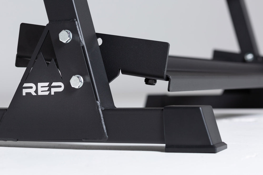 Close-up side view of the bottom of the 3-tiered matte black REP Dumbbell Rack showcasing the "REP" logo, bottom shelf, and rubber foot.